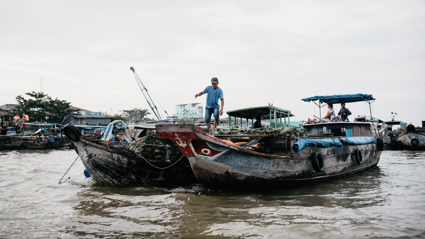 Man hopping between two boats on the Mekong River