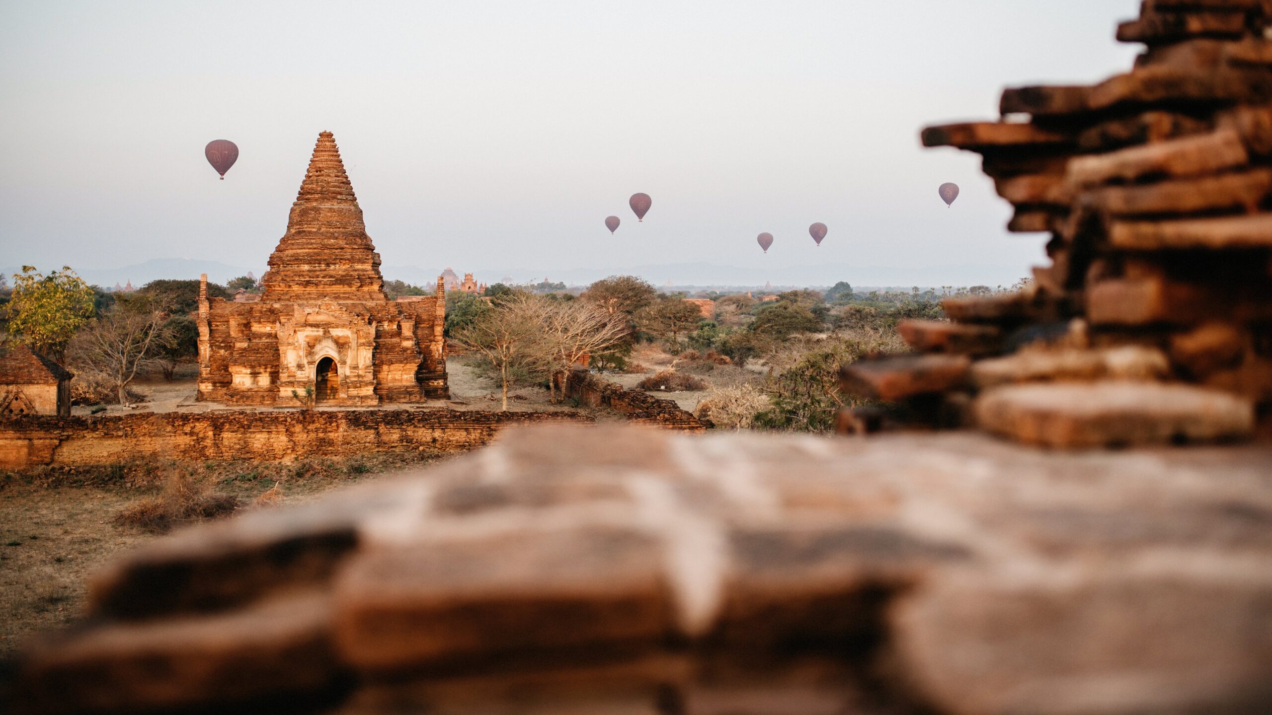 Hot-air balloons rising behind a brick pagoda at sunrise in Bagan