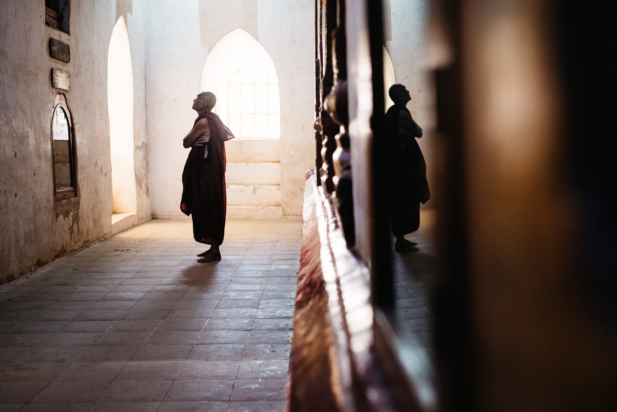 A Buddhist monk walking through a sunlit corridor inside a Bagan temple