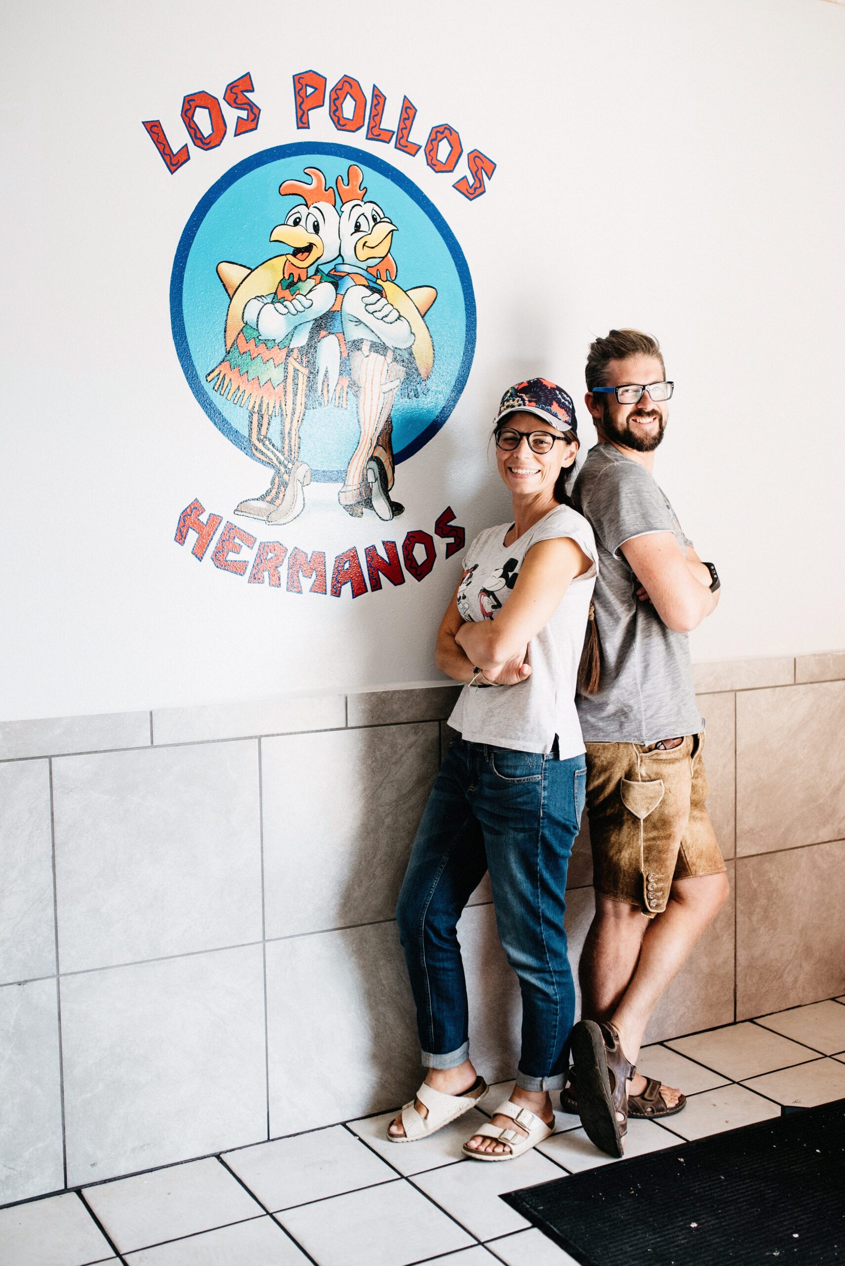 Bianca and Tom posing beneath the Los Pollos Hermanos logo