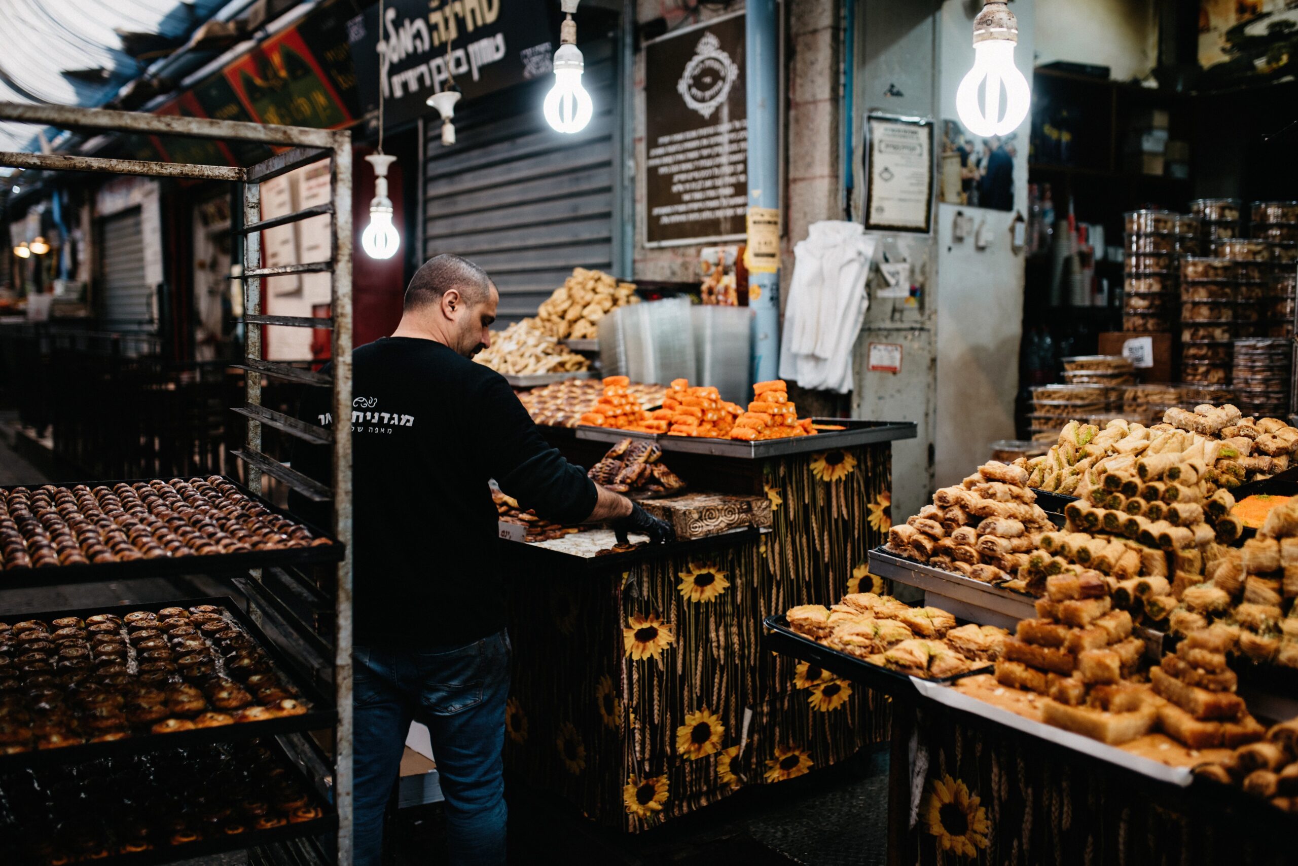A baker surrounded by trays of pastries in a Jerusalem market