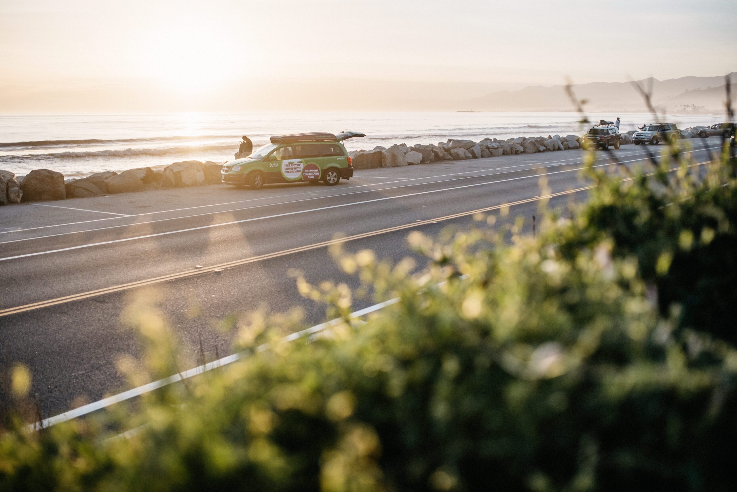 Our green JUCY campervan driving beside the Pacific Ocean