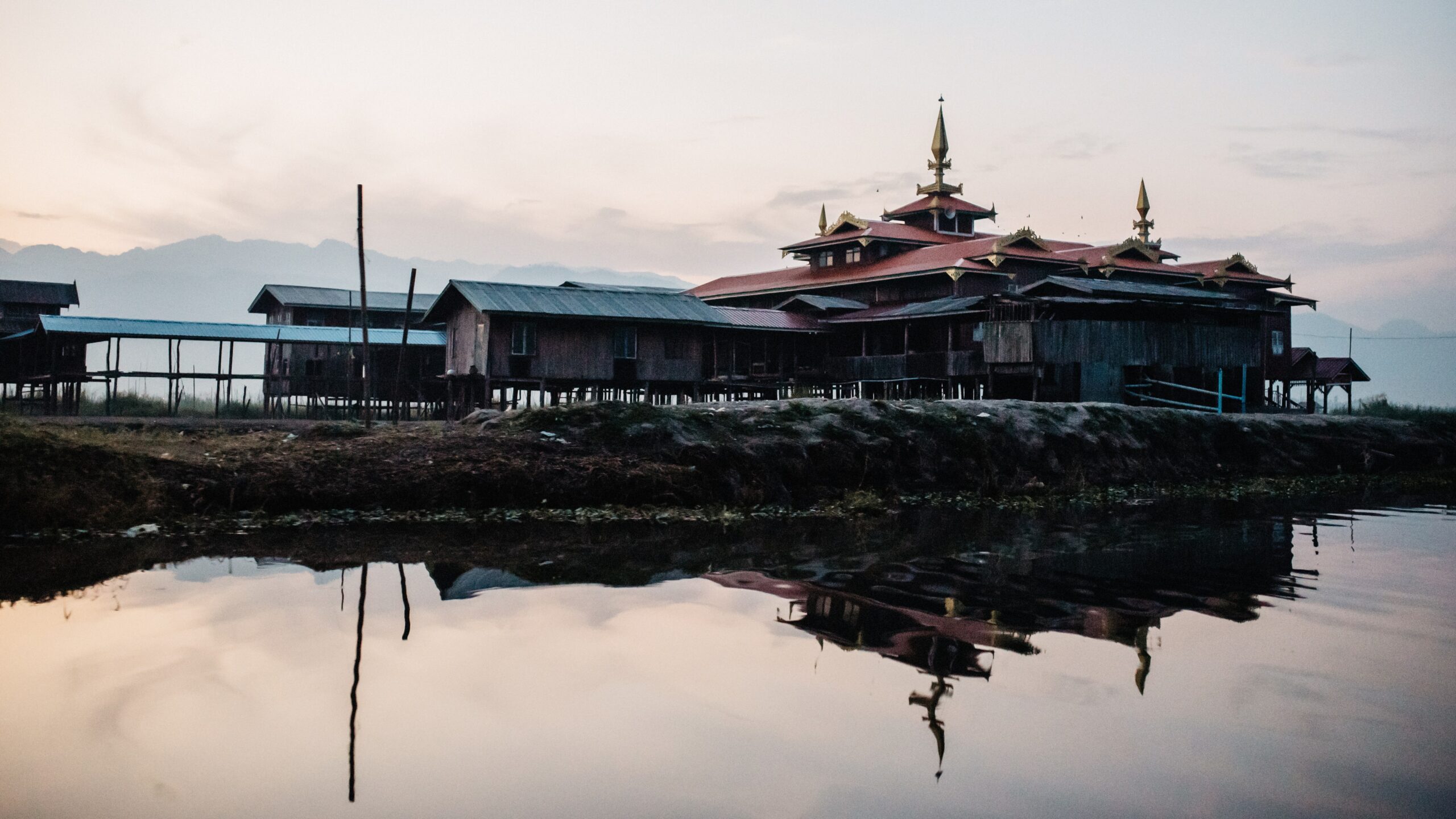 A stilted monastery reflected in the calm water of Inle Lake