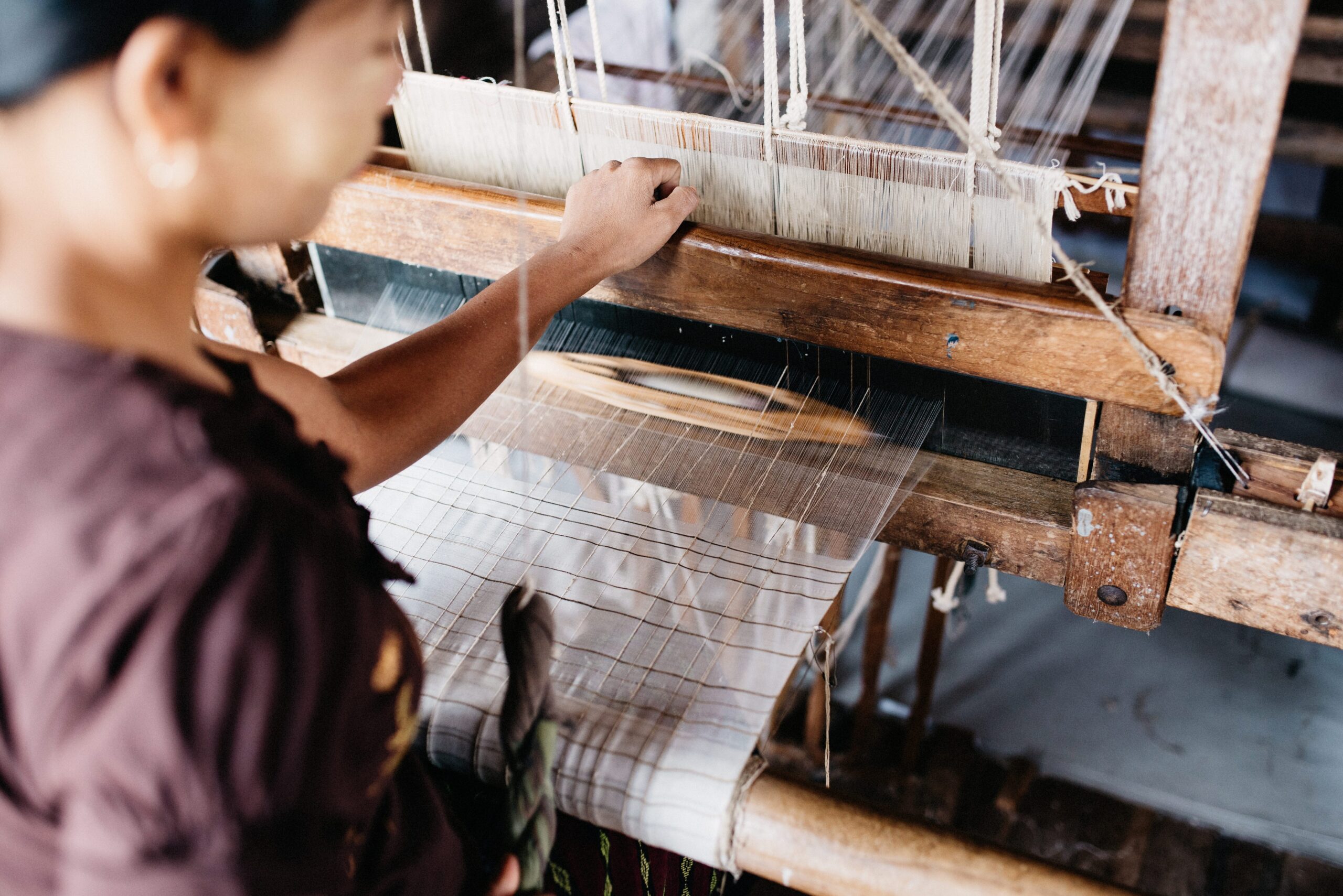 A weaver guiding thread through a wooden hand loom