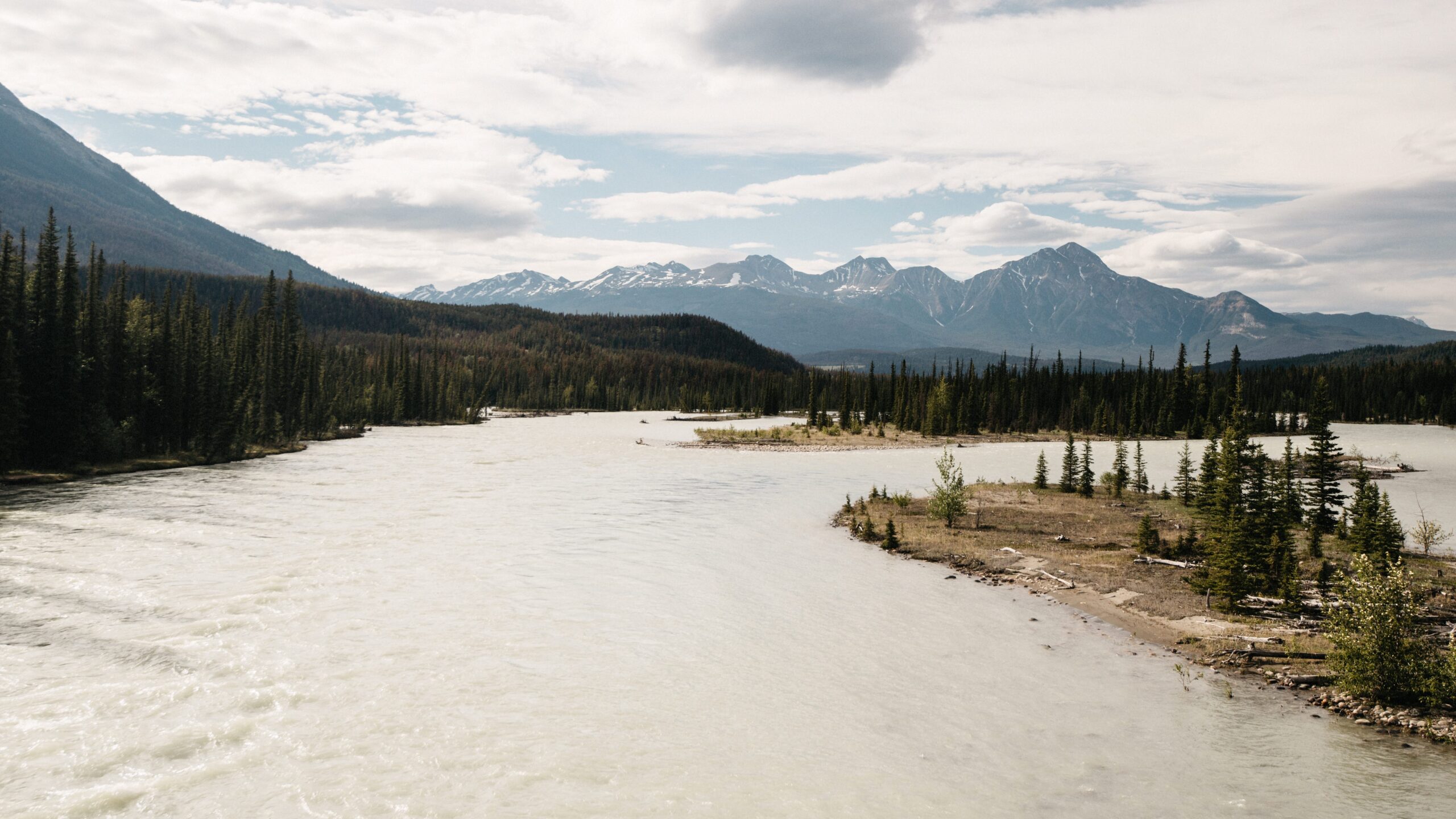 Ein breiter heller Fluss fließt durch die Berglandschaft von Jasper