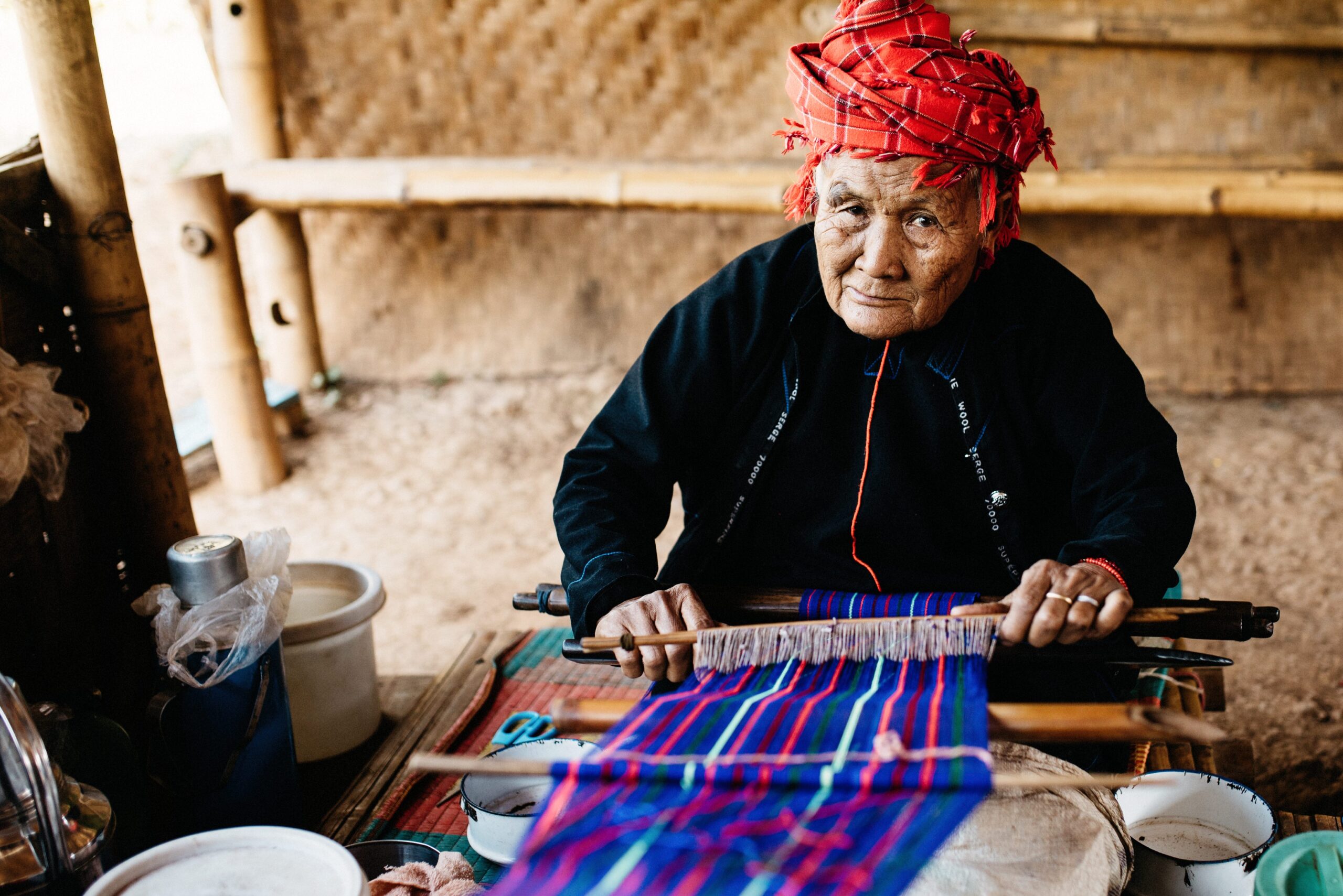 An elderly woman weaving a colourful bag in a village near Kalaw