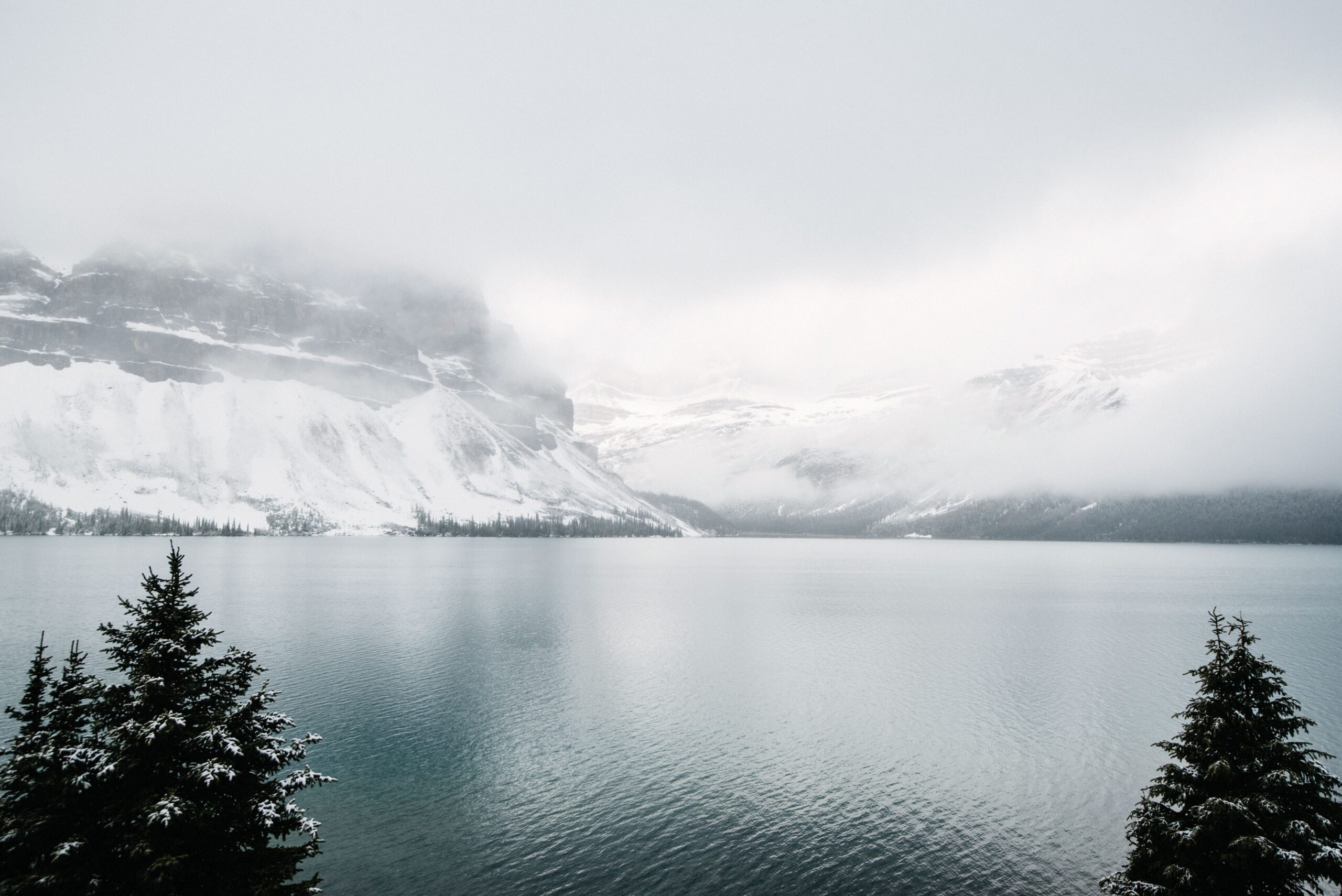 A mountain lake beneath cloud and snow-covered forest