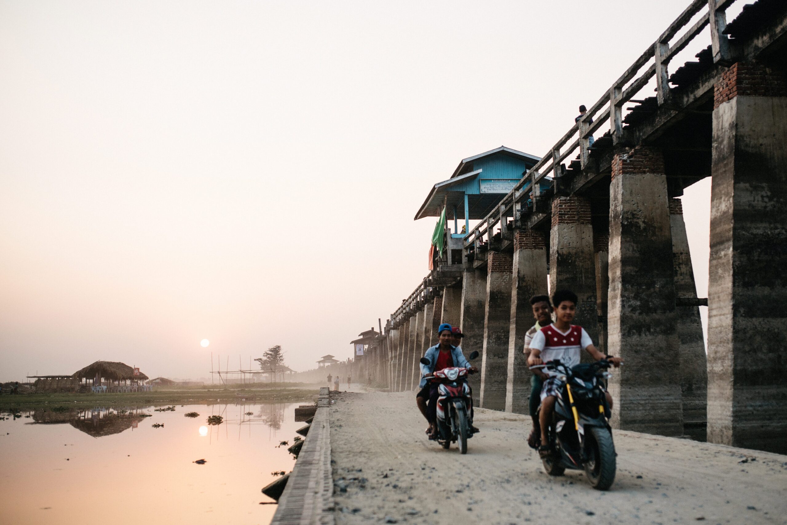 Local riders crossing beneath U Bein Bridge at sunset