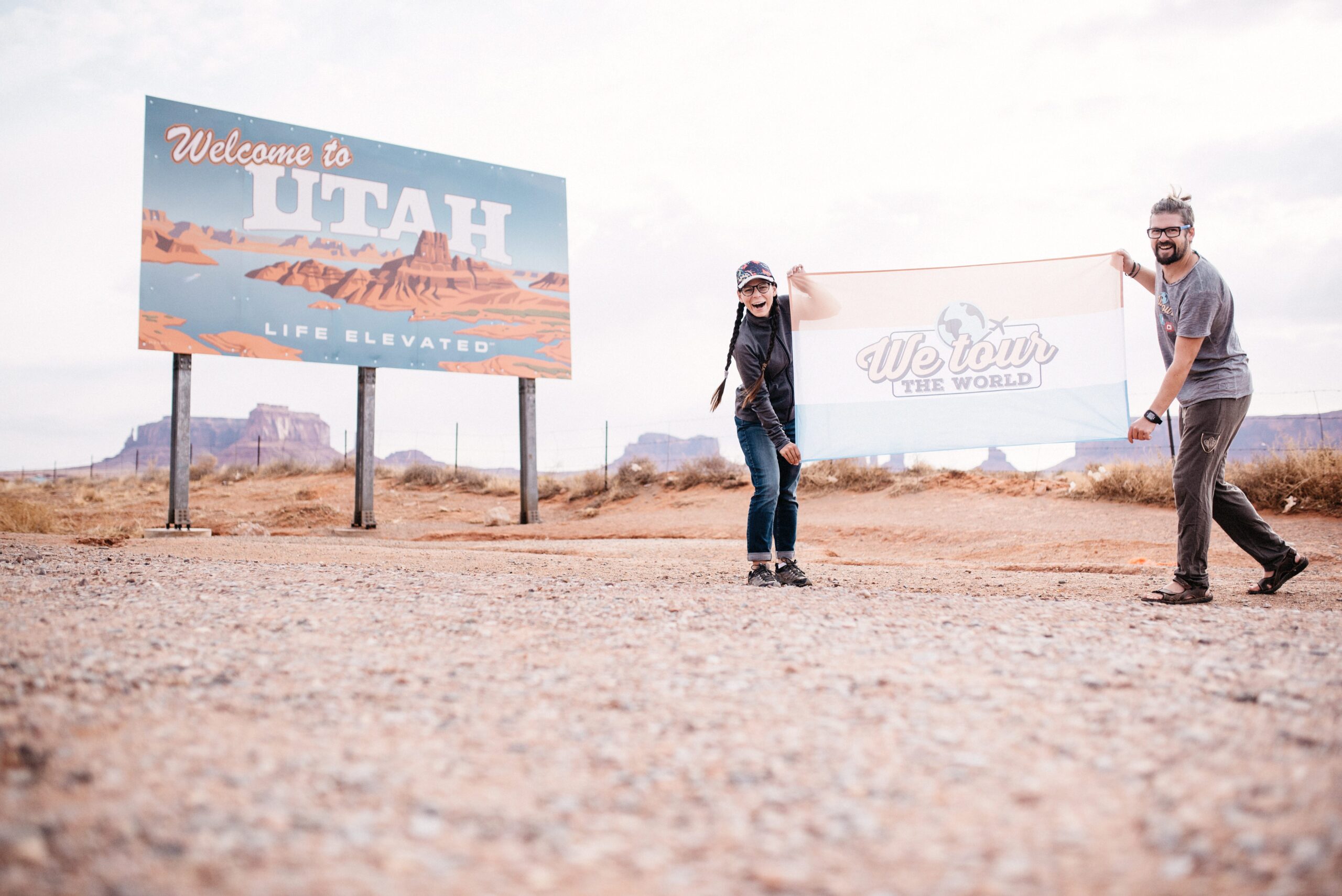 Bianca and Tom holding the We Tour The World flag at the Utah border